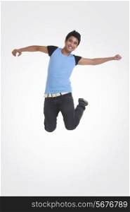 Full length portrait of young man jumping with arms outstretched over white background