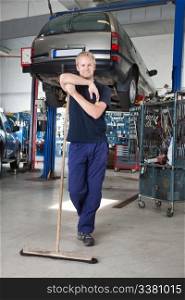 Full length portrait of young man leaning on broom in garage