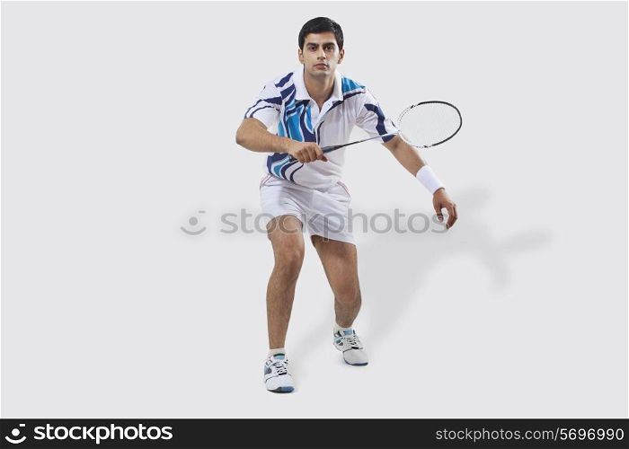 Full length portrait of young man playing badminton isolated over white background