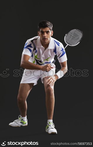 Full length portrait of young man playing badminton over black background