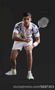 Full length portrait of young man playing badminton over black background