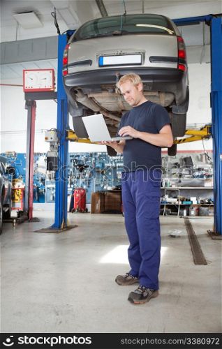 Full length portrait of young mechanic using laptop in his auto repair shop
