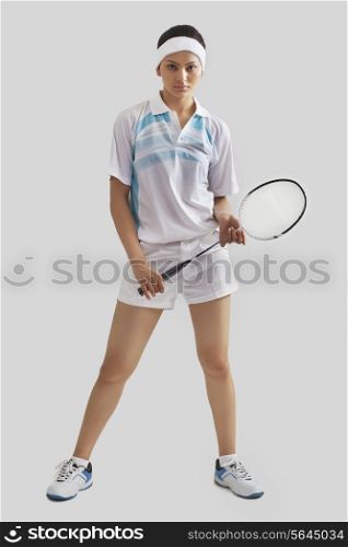 Full length portrait of young woman holding badminton racket isolated over gray background