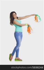 Full length portrait of young woman in casual wear holding tricolor pom poms over white background