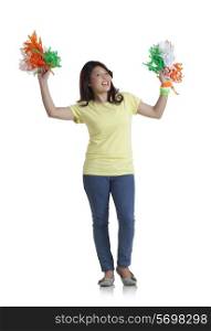 Full length portrait of young woman in casuals holding Indian tricolor pom poms over white background