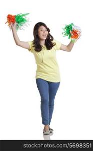 Full length portrait of young woman in casuals holding Indian tricolor pom poms over white background