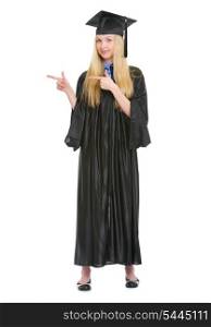 Full length portrait of young woman in graduation gown pointing on copy space