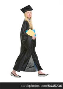 Full length portrait of young woman in graduation gown with books going sideways