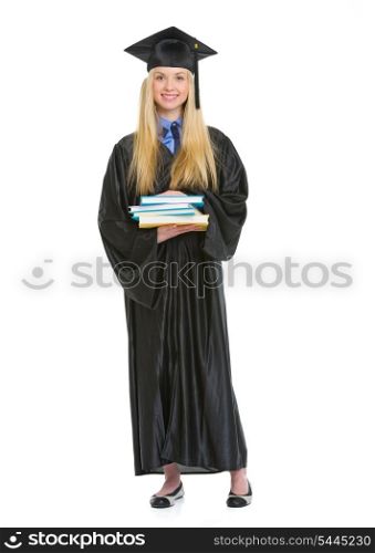 Full length portrait of young woman in graduation gown with stack of books