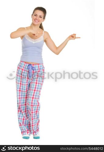 Full length portrait of young woman in pajamas pointing on copy space