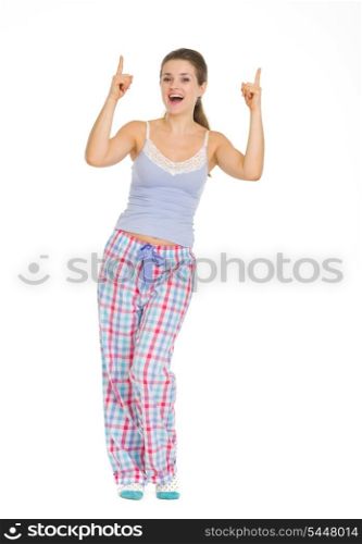 Full length portrait of young woman in pajamas pointing up on copy space