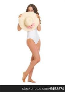 Full length portrait of young woman in swimsuit hiding behind hat