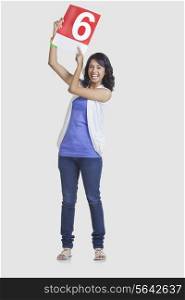 Full length portrait of young woman pointing at number 6 over white background
