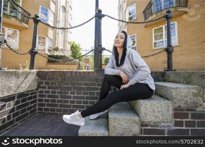 Full length portrait of young woman sitting on stairs against building