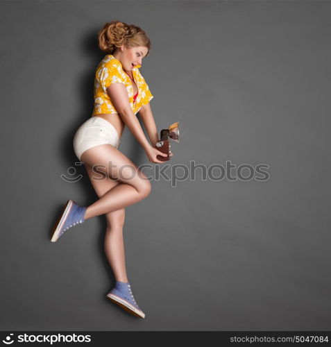 Full-length profile of a beautiful pin-up girl, holding an old vintage photo camera with bulb flash on chalkboard background.