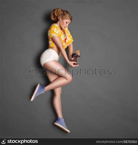 Full-length profile of a beautiful pin-up girl, holding an old vintage photo camera with bulb flash on chalkboard background.