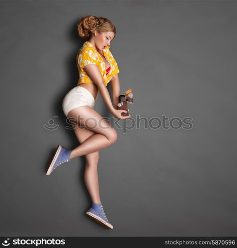 Full-length profile of a beautiful pin-up girl, holding an old vintage photo camera with bulb flash on chalkboard background.