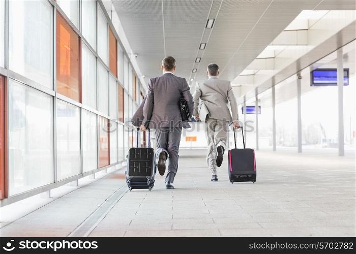 Full length rear view of businessmen with luggage running on railroad platform