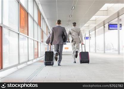 Full length rear view of businessmen with luggage running on railroad platform