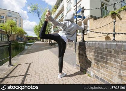 Full length rear view of fit woman performing stretching exercise on sidewalk