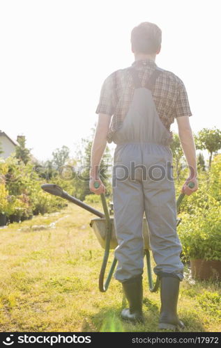 Full-length rear view of gardener pushing wheelbarrow at garden
