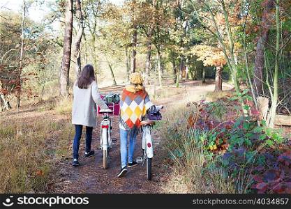 Full length rear view of teenage girls walking in forest pushing bicycles