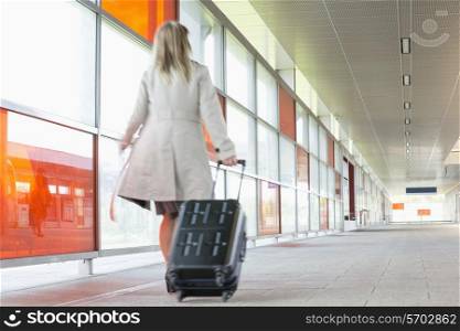 Full length rear view of young businesswoman with luggage rushing in railroad station