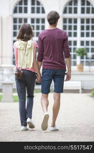 Full-length rear view of young couple walking against building