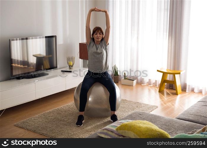 Full length shot of a woman doing exercise at home with a swiss Ball