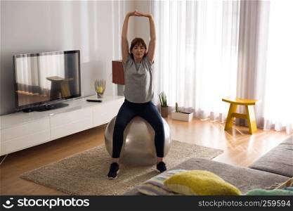 Full length shot of a woman doing exercise at home with a swiss Ball