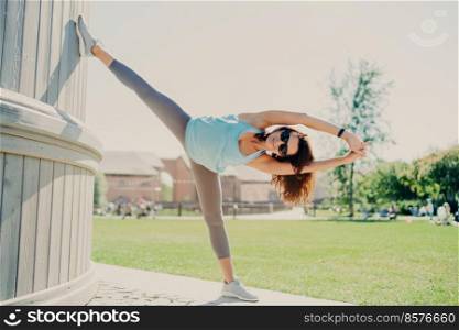 Full length shot of active woman stretches legs and arms stays always in good physical shape has perfect flexibility sporty body wears cropped top leggings and sneakers. Sport lifestyle concept