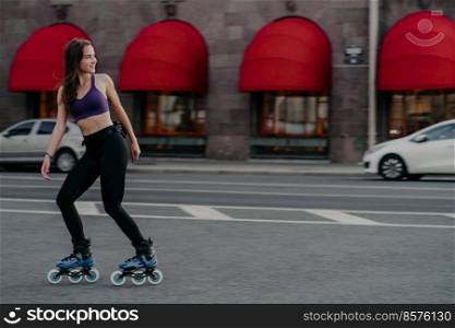 Full length shot of slim active young woman rides rollerblades for strong muscles enjoys favorite hobby has good exercises for figure and health improves muscular endurance increases strength