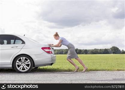 Full length side view of businesswoman pushing broken down car at countryside
