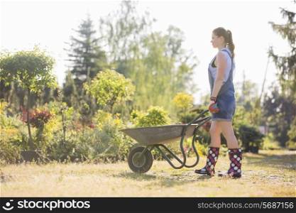 Full-length side view of female gardener pushing wheelbarrow at plant nursery
