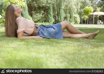 Full length side view of relaxed young woman lying on grass in park