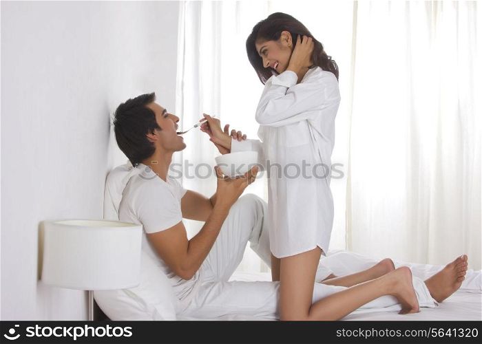 Full length side view of romantic woman feeding man in bed