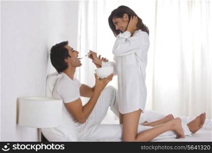 Full length side view of romantic woman feeding man in bed