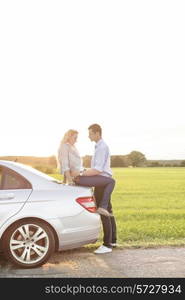 Full length side view of romantic young couple by car at countryside