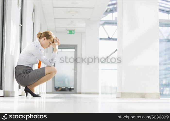 Full-length side view of stressed businesswoman crouching at office hallway