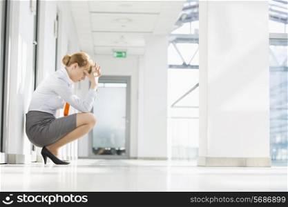 Full-length side view of stressed businesswoman crouching at office hallway