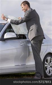 Full length side view of young businessman reading map by car at countryside