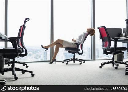 Full length side view of young businesswoman leaning back in chair at office