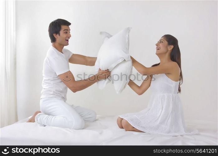 Full length side view of young couple having pillow fight on bed