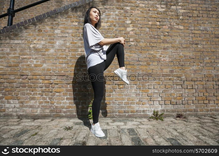 Full length side view of young fit woman stretching against brick wall