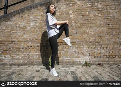 Full length side view of young fit woman stretching against brick wall