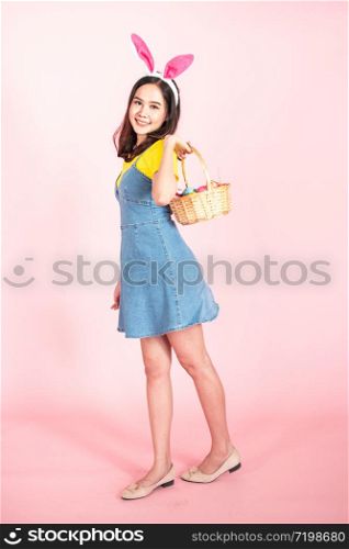 full length studio shot of asian beauty happy young woman wearing bunny ears and holding colorful Easter egg in wood basket with lovely smile and colorful decor costume isolated on pastel backgrounds.