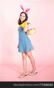 full length studio shot of asian beauty happy young woman wearing bunny ears and holding colorful Easter egg in wood basket with lovely smile and colorful decor costume isolated on pastel backgrounds.