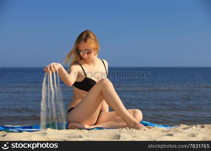 Full length woman in bikini at the sandy beach pouring fine sand