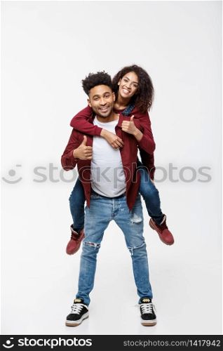 Full length young attractive african american lady riding back on her boyfriend back and showing thumb up. Full length young attractive african american lady riding back on her boyfriend back and showing thumb up.