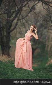 full length young stylish woman near blossoming tree in the spring park. blonde girl with hairstyle in pink dress. selective focus. full length young stylish woman near blossoming tree in the spring park. blonde girl with hairstyle in pink dress